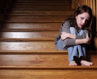 Young girl looking upset sat on staircase