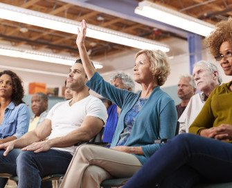 People sat at a public meeting with hands raised