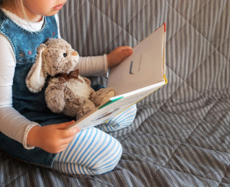 Little girl kneeling reading with a teddy
