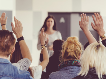 Audience with hands raised facing female speaker