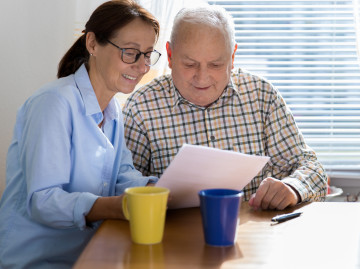 lady helping an older male to read a piece of paper sat at a table
