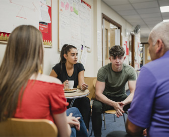 Young people sitting around a table talking to an adult