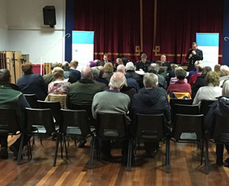 Backs of a room full of people sat at a meeting in a hall